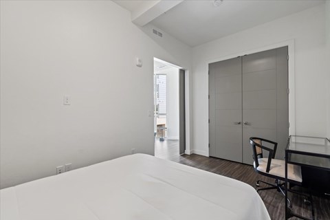 A white bed in a room with a chair and a table.