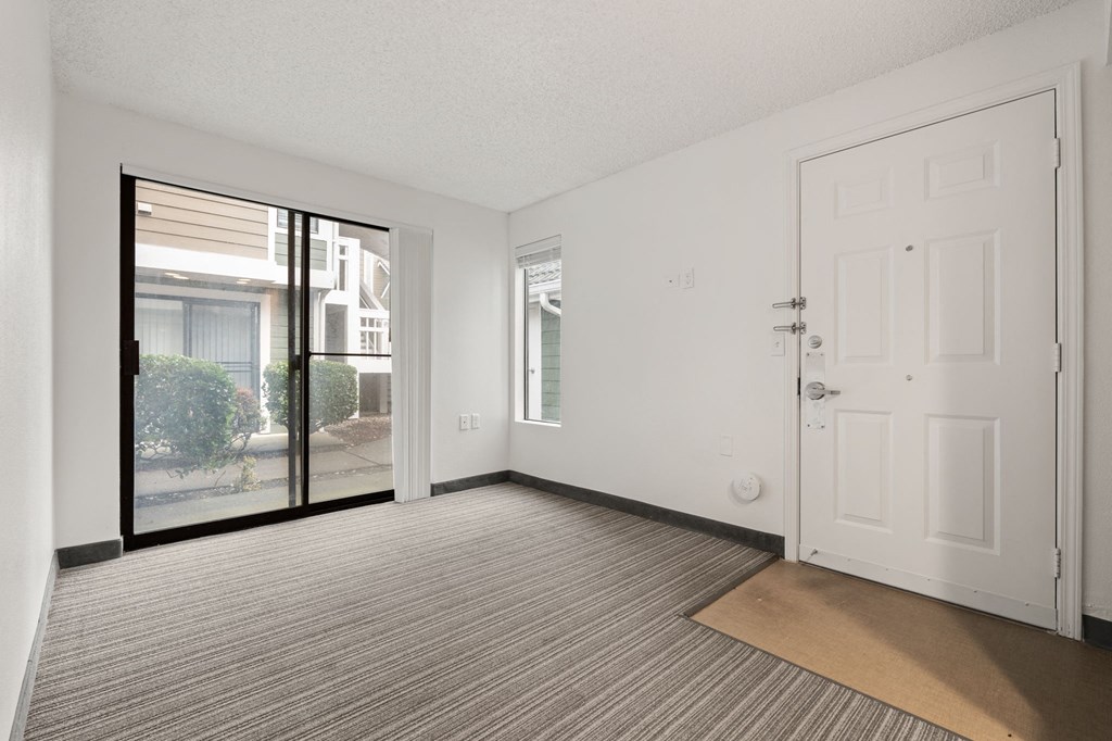 A room with a carpeted floor, a white door, and a sliding glass door leading to a balcony. at AVIA Lofts on Parkway Apartments, Vancouver, Washington