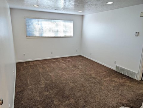 A room with a carpeted floor and a window with blinds.