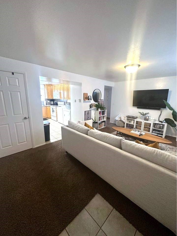 A living room with a white couch and a flat screen TV mounted on the wall.