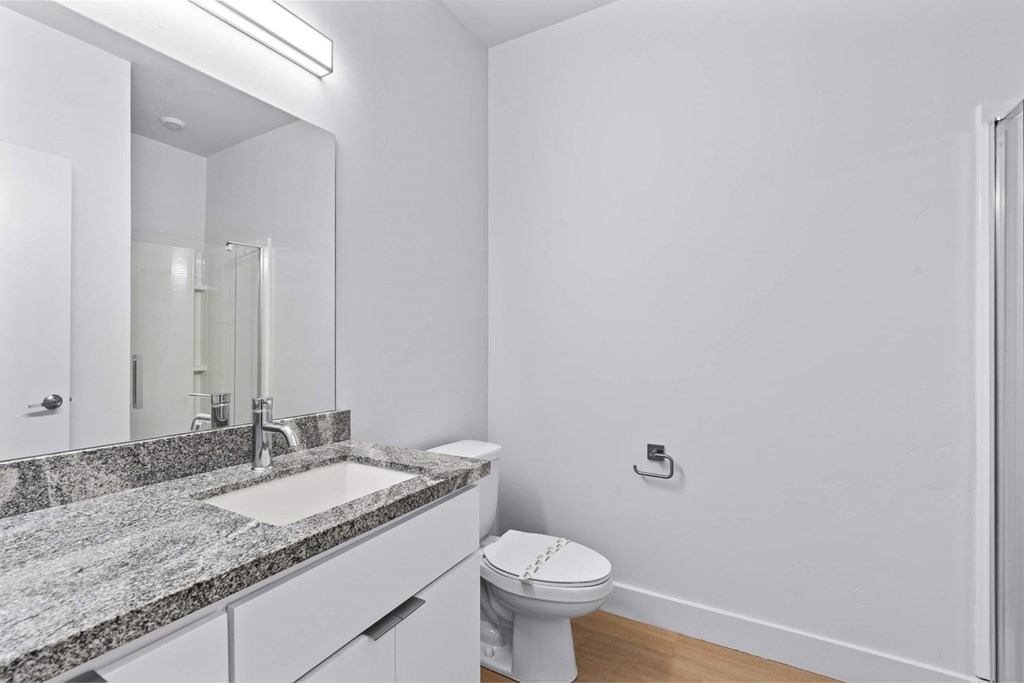 A bathroom with a toilet, sink, and mirror. at Brickside Heights, Millcreek, Utah
