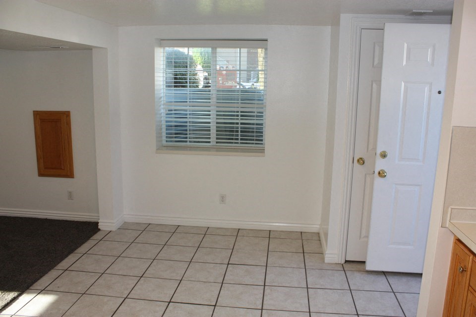 A room with a white door, a window with blinds, and a tiled floor.