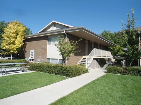 A building with a brown roof and a white awning is surrounded by greenery.
