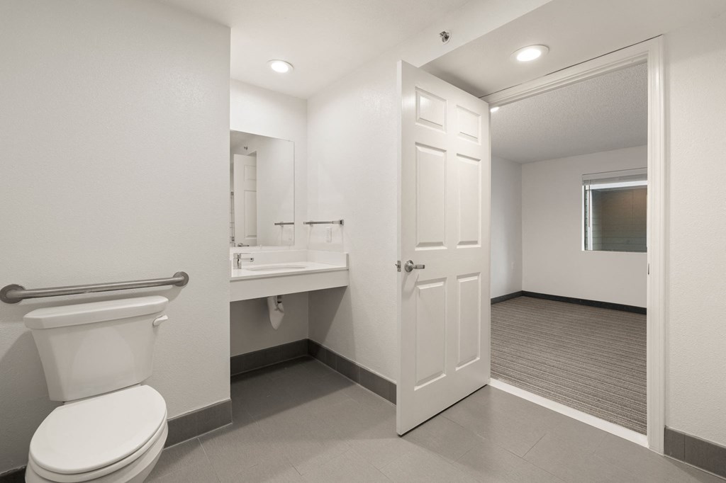 A white toilet is in a small bathroom with a white sink and a white door at AVIA Lofts on Parkway Apartments, Vancouver, WA, 98662