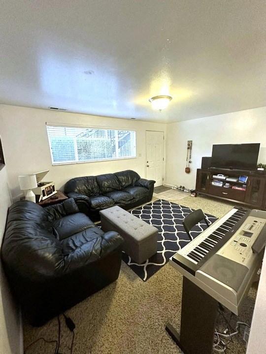 A black leather couch sits in a living room with a piano in the corner.