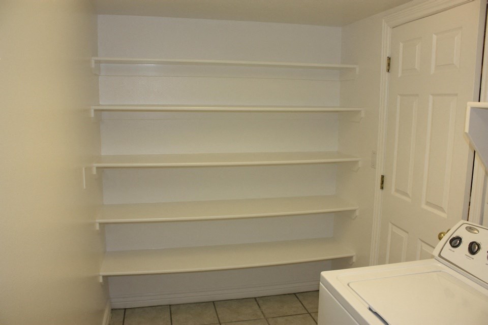 A white washing machine sits in a laundry room with a white door and shelves.