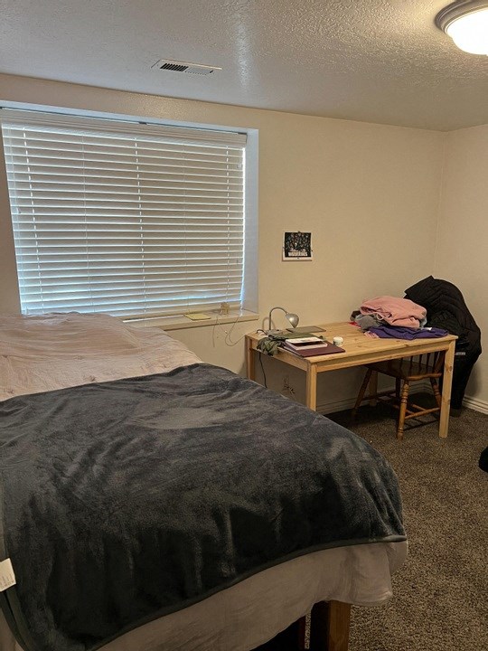 A bedroom with a bed, desk, and window with blinds.
