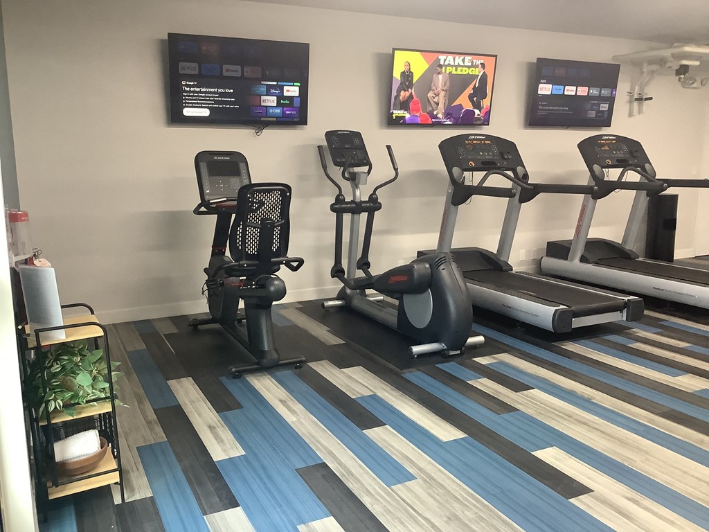 a gym with four exercise machines and a tv on the wall