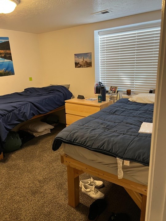 A bedroom with two beds, one of which is made up with a blue comforter.