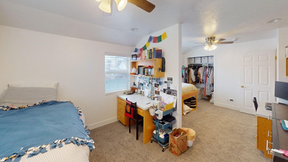 A bedroom with a bed, desk, and a fan.