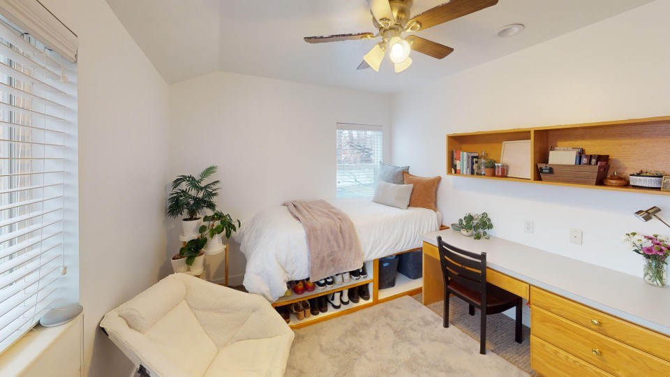 A bedroom with a bed, chair, and a ceiling fan.