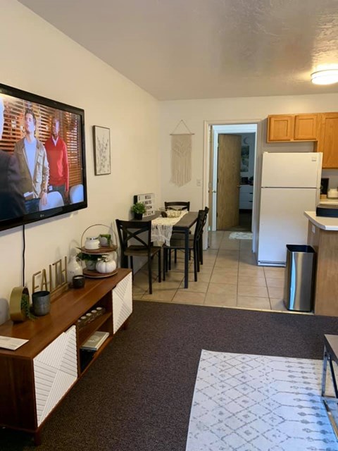A kitchen with a refrigerator, a dining table with chairs, and a TV mounted on the wall.