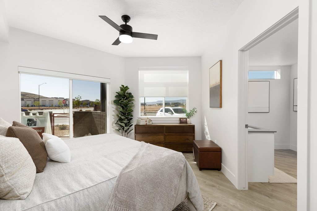 A bedroom with a bed, a ceiling fan, and a window overlooking a street.