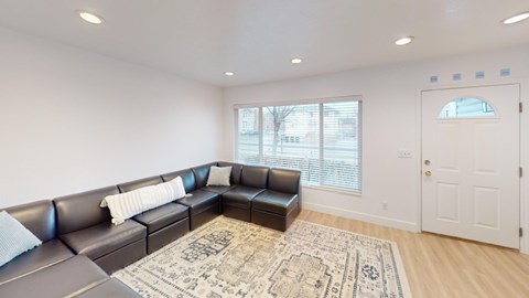 A living room with a black leather couch and a rug.
