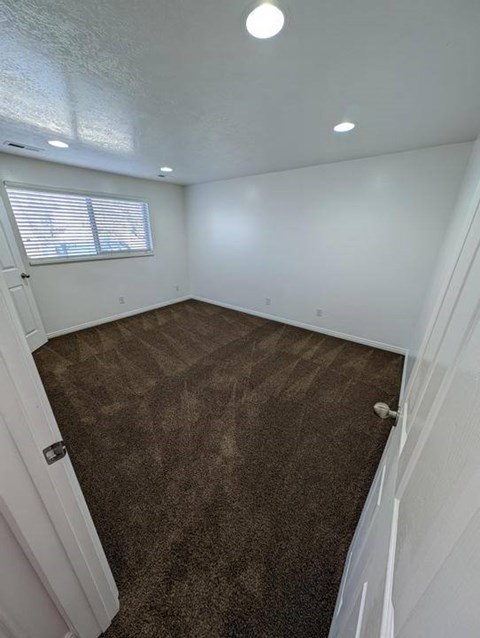 A room with brown carpet and a window with blinds.