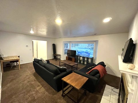 A living room with a black couch and a television on the wall.