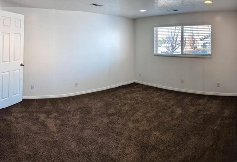 A room with brown carpet and a window with blinds.