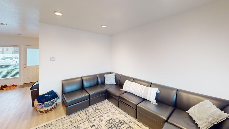 A black leather couch with a white pillow and a basket on the floor.