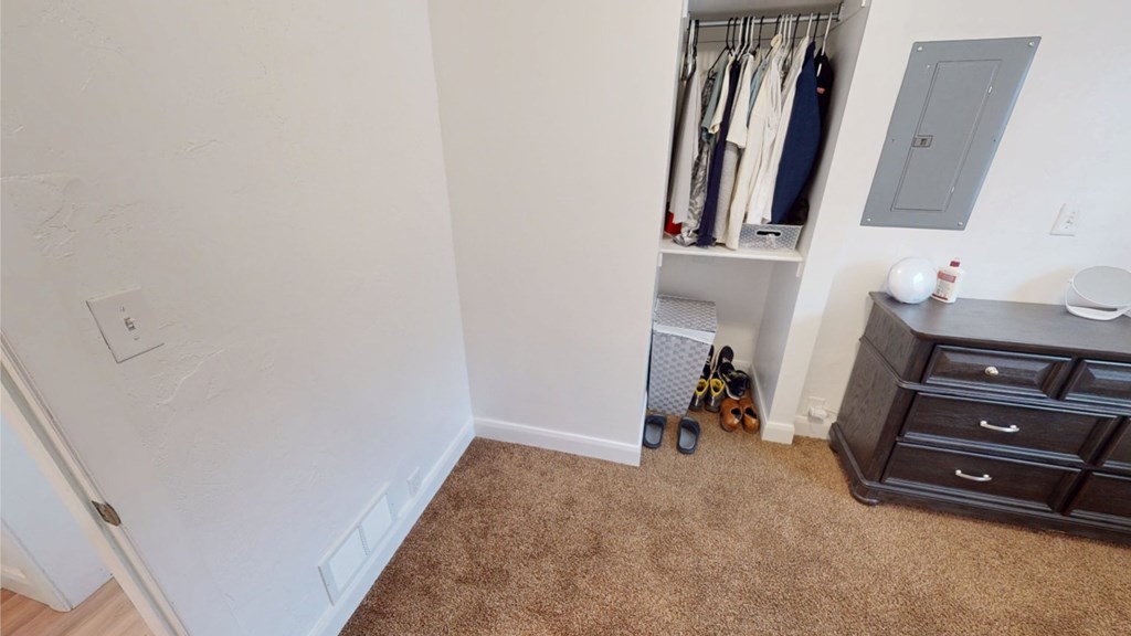 A room with a carpeted floor and a closet with clothes hanging.