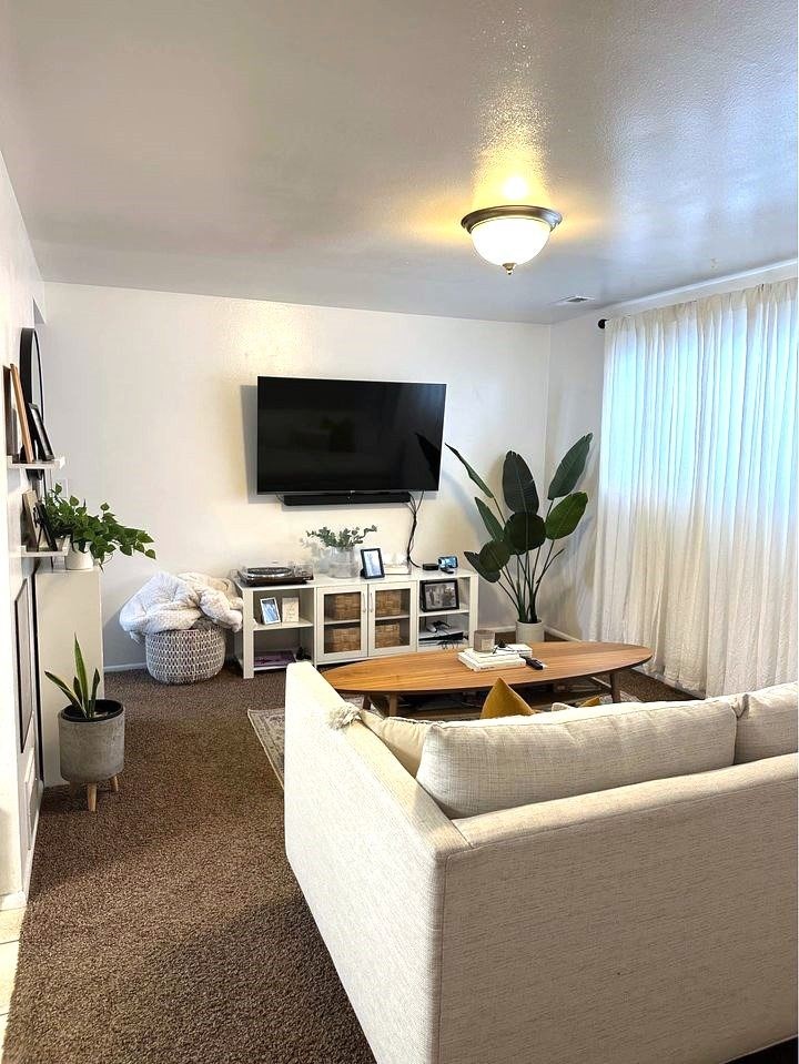 A living room with a white couch and a flat screen TV mounted on the wall.