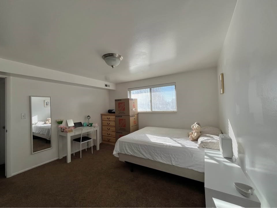 A bedroom with a bed, desk, and mirror.