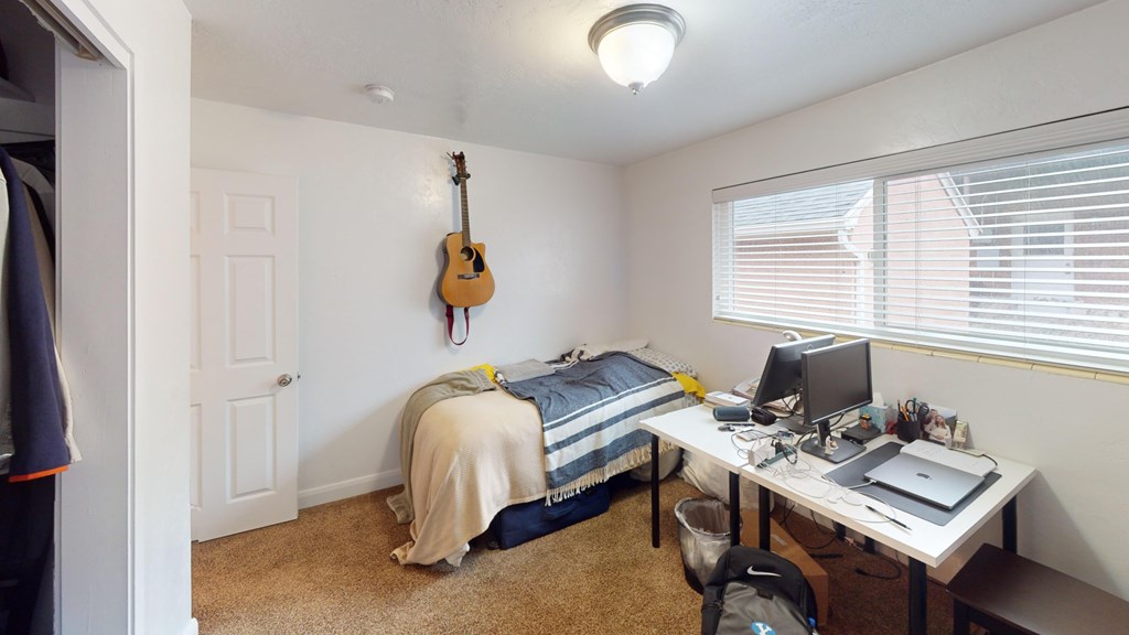 A room with a bed, desk, and a guitar hanging on the wall.