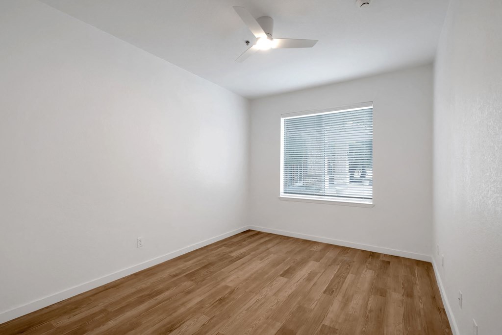 a bedroom with white walls and wood floors and a window