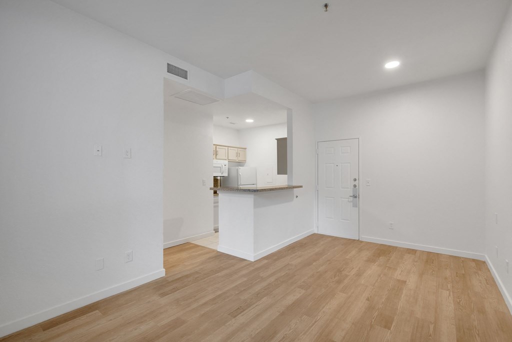 a living room and kitchen with white walls and wood flooring