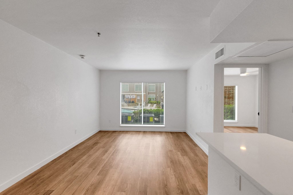 the living room and dining room of an apartment with wood floors and a large window