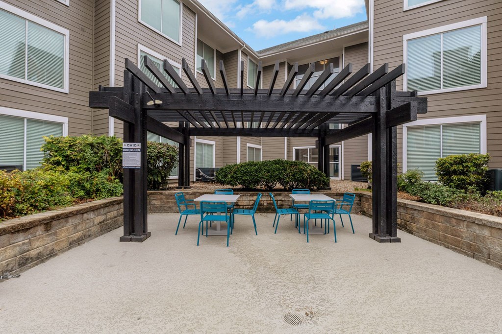 a patio with blue tables and chairs under a wooden pergola