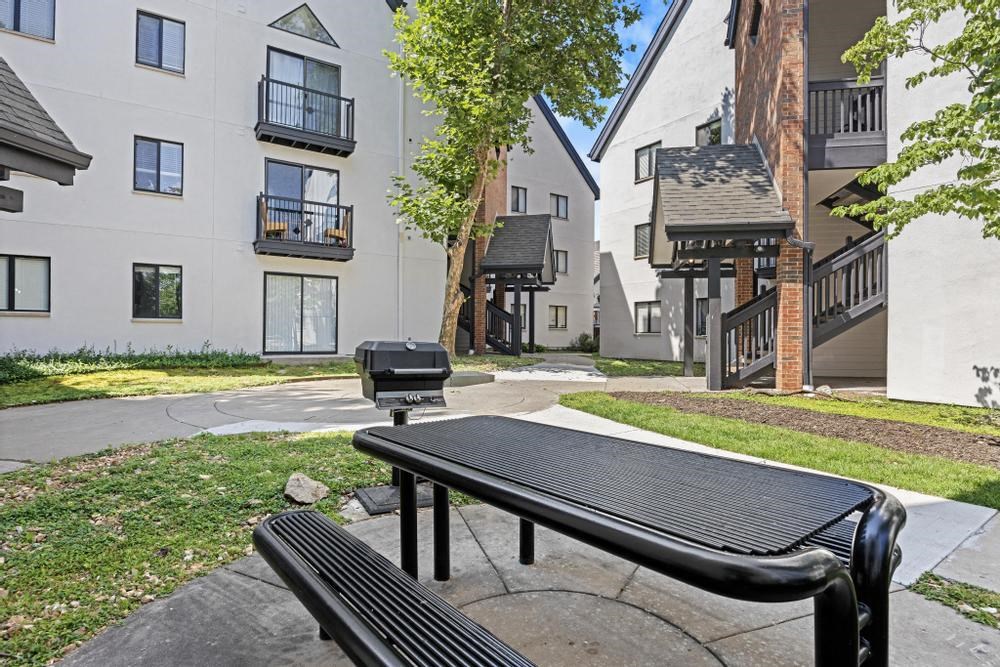 a picnic area with two benches and a grill in front of an apartment building