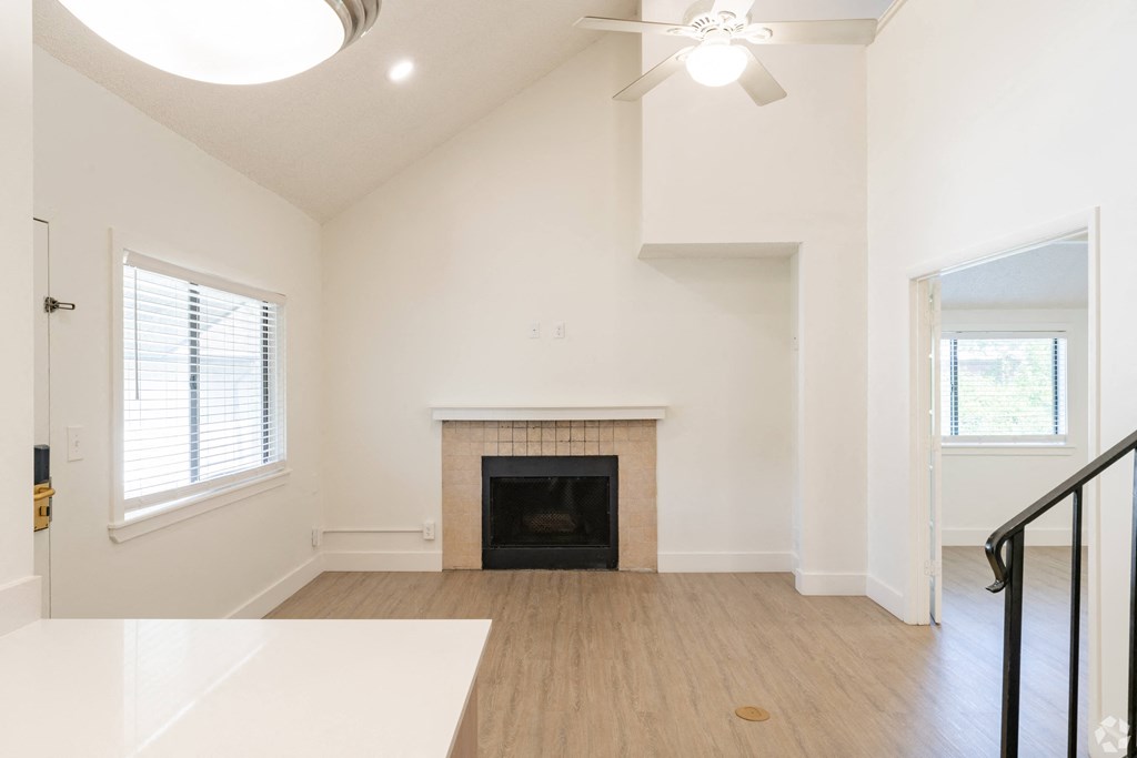 an empty living room with a fireplace and a ceiling fan