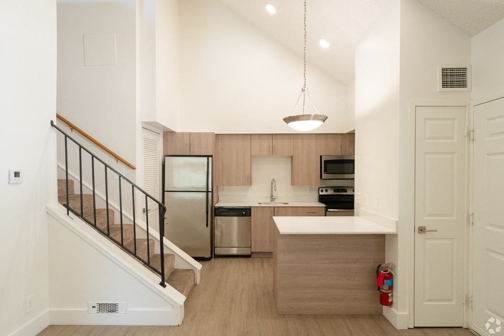 a white kitchen with a staircase and a stainless steel refrigerator