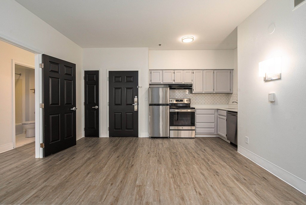 an empty living room and kitchen with black doors and stainless steel appliances