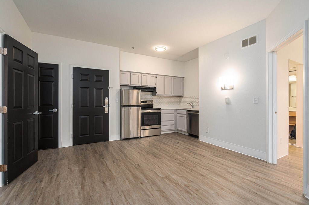 an empty living room and kitchen with a wood floor and black doors