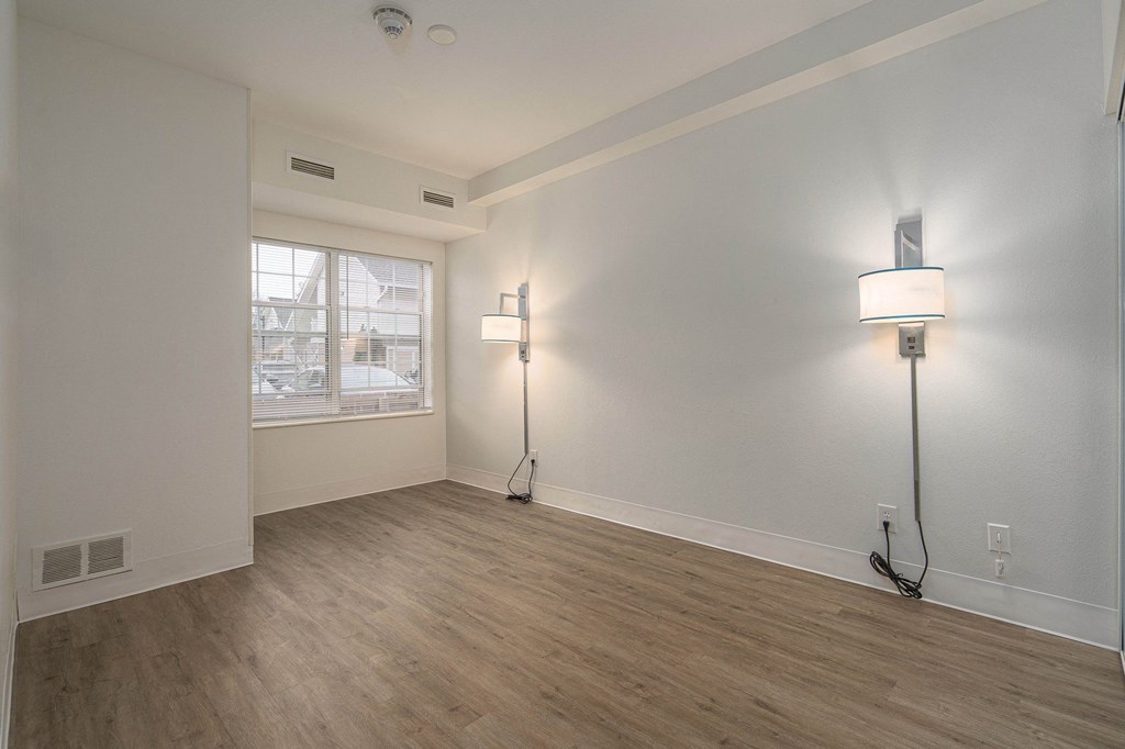 an empty living room with a window and two floor lamps