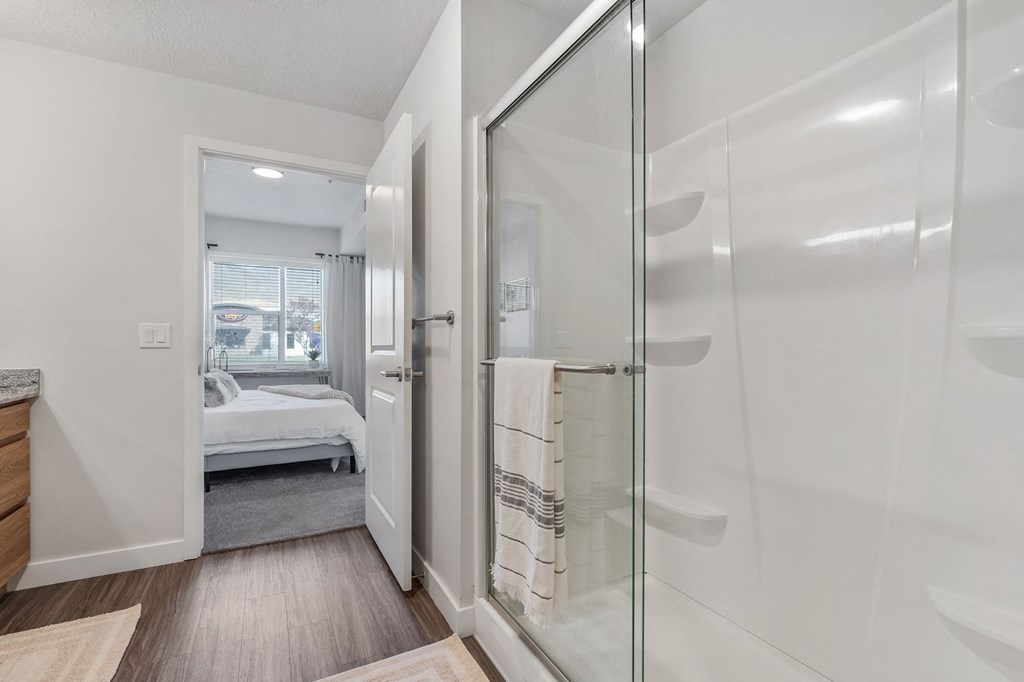 a white bathroom with a glass shower and a bedroom at The Flats at Riverwoods, Provo, Utah