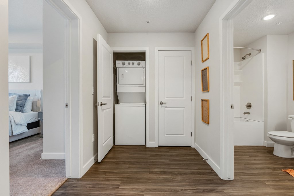 a hallway with a toilet and a washer and dryer in a white room at The Flats at Riverwoods, Provo, UT, 84604