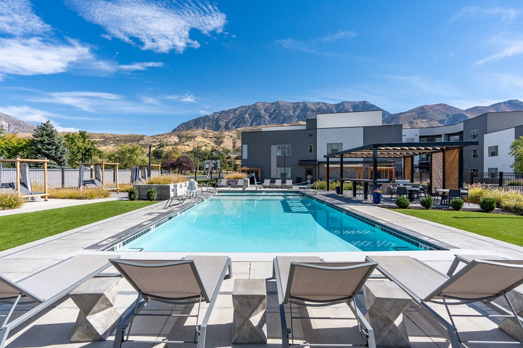 a swimming pool with chairs and a building in the background at The Flats at Riverwoods, Provo, UT, 84604