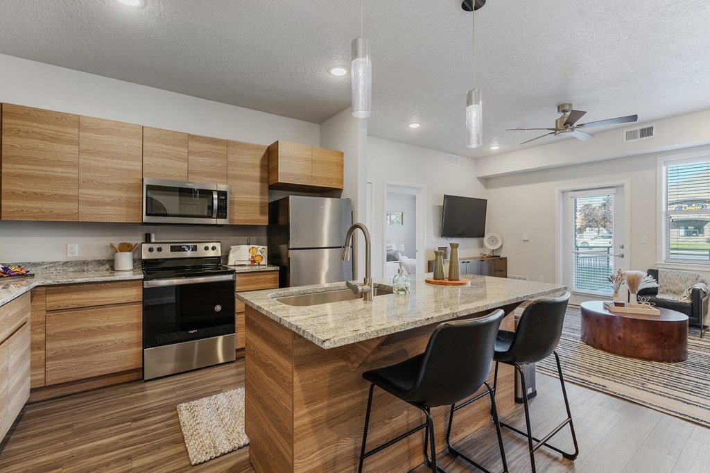 a kitchen with a marble counter top and an island with chairs at The Flats at Riverwoods, Provo, UT