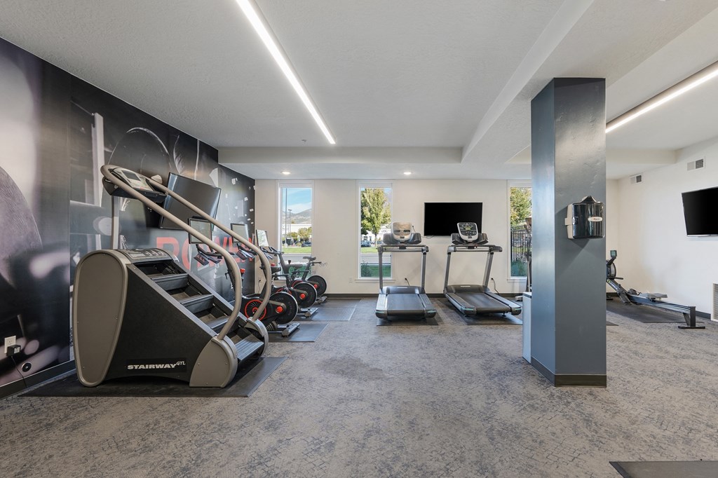 a gym with treadmills and other exercise equipment in a room with a tv at The Flats at Riverwoods, Provo, UT, 84604