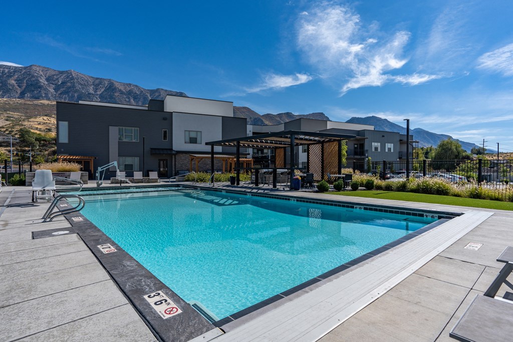 a swimming pool with a building in the background and a blue sky at The Flats at Riverwoods, Provo, UT
