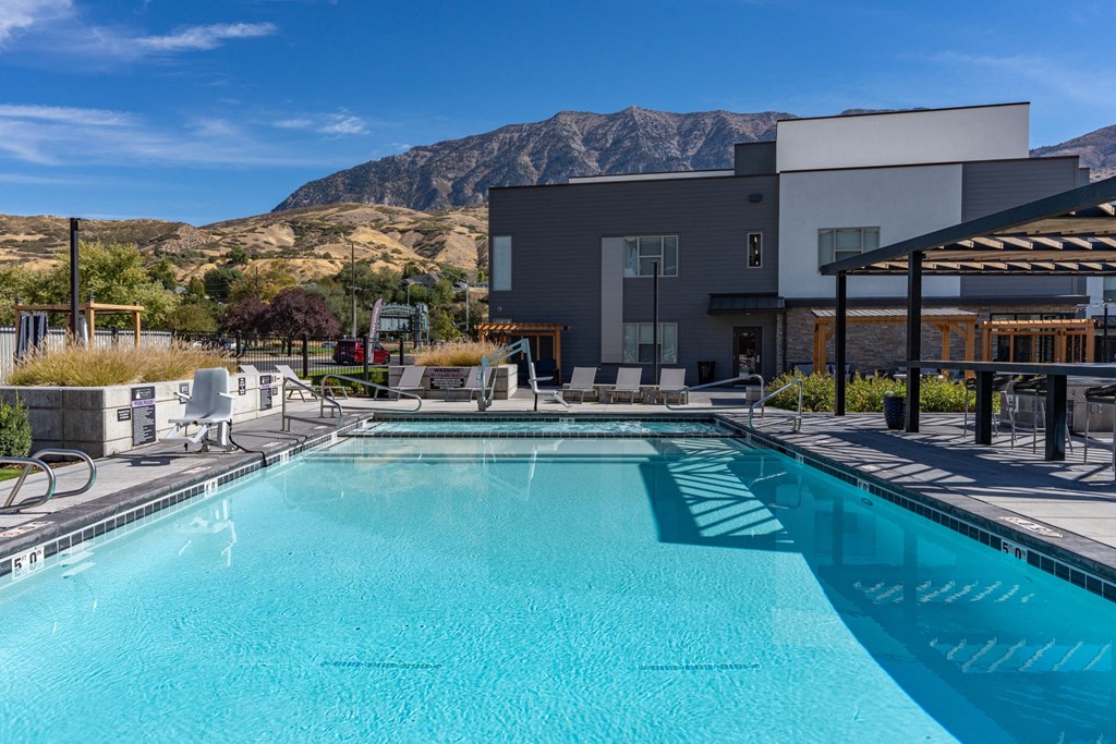 a swimming pool with a building and mountains in the background at The Flats at Riverwoods, Provo