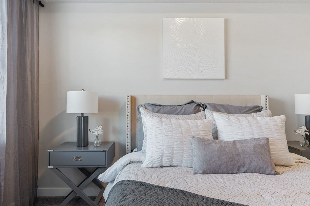 a bedroom with a bed and pillows and a nightstand with a lamp and at The Flats at Riverwoods, Provo, UT, 84604