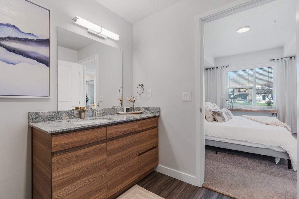 a bathroom with a vanity and a mirror and a bedroom with a bed at The Flats at Riverwoods, Provo, 84604