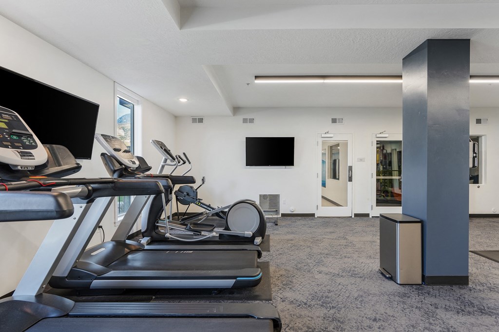the gym has cardio equipment and a flat screen tv at The Flats at Riverwoods, Provo, UT, 84604