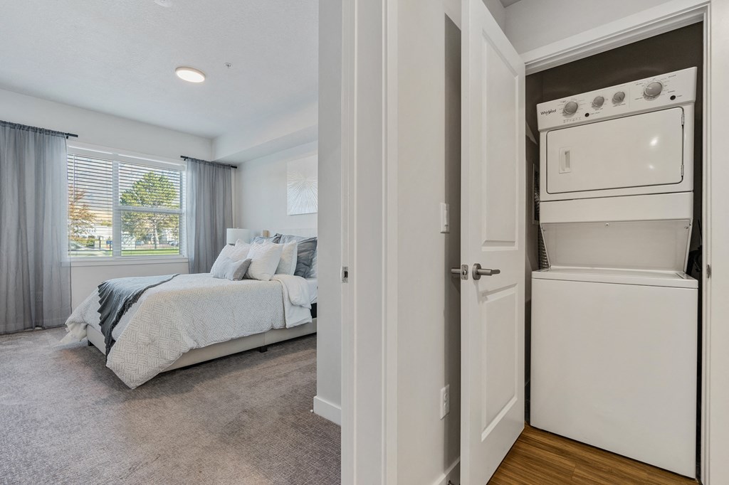 a bedroom with a bed and a washer and dryer next to a closet at The Flats at Riverwoods, Provo, Utah