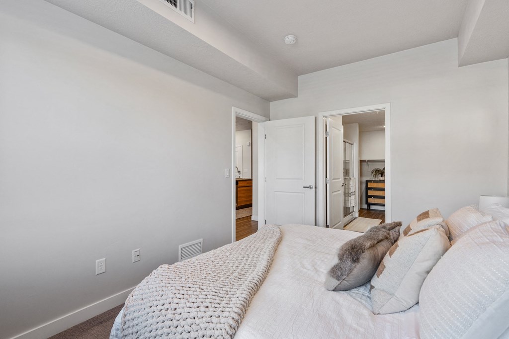 a bedroom with a large bed and a door to a bathroom at The Flats at Riverwoods, Provo