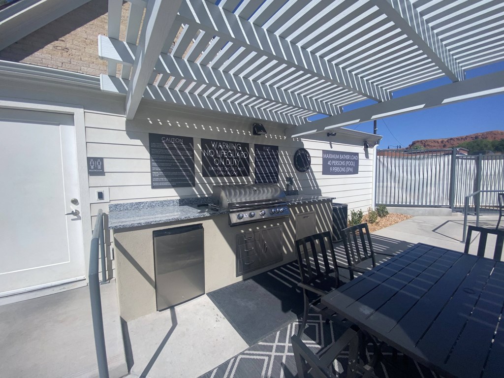 the outdoor kitchen has a grill and a table with chairs
