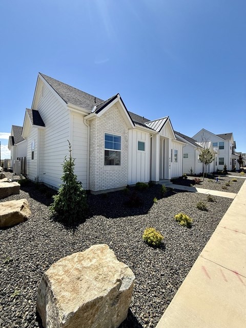 A white house with a grey roof and a gravel garden in front at Alante Homes at Spring Run Flats Apartments, Idaho